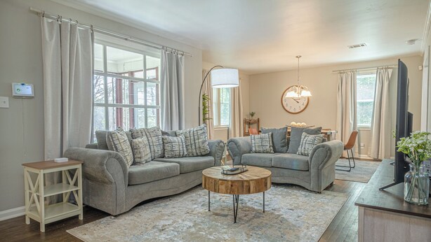 A living room with two grey sofas, a wooden coffee table, a side table, and a TV stand with a vase of flowers. - Charming Spacious Home with Game room (Columbus)