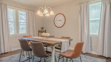 A dining room with a wooden table, six chairs, a clock, and a chandelier.