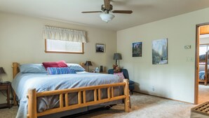 A bedroom with a wooden bed, a ceiling fan, a window with blinds, and two wall-mounted paintings. - Amazing 3-bedroom Home in Beautiful Blue Lake Springs, Arnold California (Arnold)