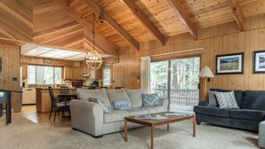 A spacious living area with a sofa, a coffee table, and a dark-colored couch. A kitchen is visible in the background with a dining area. - Amazing 3-bedroom Home in Beautiful Blue Lake Springs, Arnold California (Arnold)