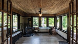 L’intérieur chaleureux d’un chalet avec une cheminée en pierre, un plancher en bois et de grandes fenêtres donnant sur le paysage extérieur.