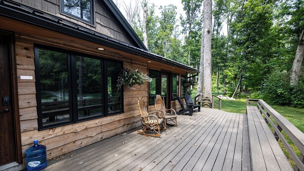 Une cabane en bois dotée de grandes fenêtres, d’une terrasse avec des chaises et d’un panneau indiquant qu’il est interdit d’y introduire des animaux de compagnie.