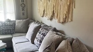 A living room with a grey sofa, patterned cushions, and a macramé wall hanging.