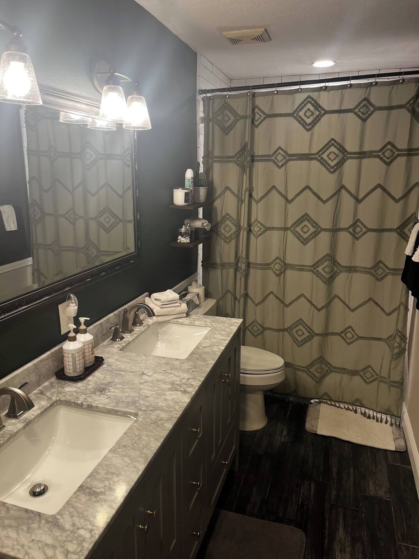 Une salle de bain avec un double lavabo, des toilettes et un rideau de douche à motifs géométriques.