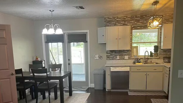 A spacious living area with a dark wooden floor, a dining table with chairs, a kitchen with white cabinets, and a large window providing natural light.