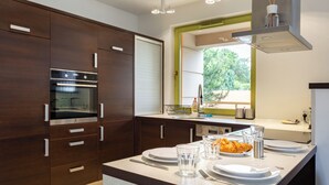 A modern kitchen with dark wood cabinets, a built-in oven, a window with a view of greenery, and a breakfast setup on the counter.