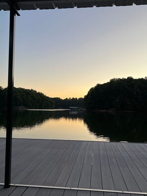 Eine Holzterrasse mit Blick auf einen stillen See, dessen Ufer von einem Wald gesäumt wird, und ein kleiner Steg in der Ferne.