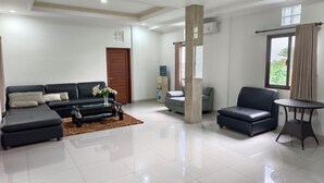 A spacious living room with a sectional sofa, a small round table, and a grey armchair. - Ayuna Guest House – Comfortable & Affordable in Bali (Bali)
