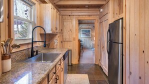 A wooden kitchen with granite countertops, a stainless steel refrigerator, and a window with a view of trees. - Cozy Mountain Cabin w/ Creek, near Dining & Hiking (Monteagle)