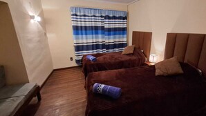 Une chambre d'hôtel avec deux lits, un canapé, une fenêtre avec des rideaux à rayures et un lampadaire fixé au mur.
