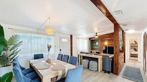 A spacious dining area with a wooden table and blue upholstered chairs, a kitchen area with wooden cabinets, and a large window with blinds. - 3BR Largo Retreat w/ Private Pool & Patio (Largo)