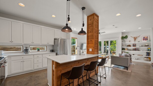 A modern kitchen with white cabinets, a wooden accent wall, and a central island with bar stools. - Group-Friendly 4BR | Steps from East Austin Fun (Austin)