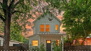 A two-story house with a front porch, a picket fence, and a tree in the foreground. - Group-Friendly 4BR | Steps from East Austin Fun (Austin)