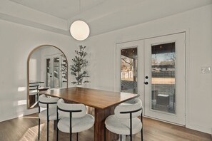 A dining area with a wooden table and four chairs, a large mirror, and a potted plant.