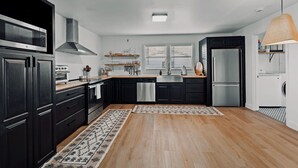 A modern kitchen with black cabinets, stainless steel appliances, and a wooden floor. - NEW! Charcoal & Charm!! (Spring Hill)