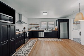 A modern kitchen with black cabinets, stainless steel appliances, and a wooden floor.