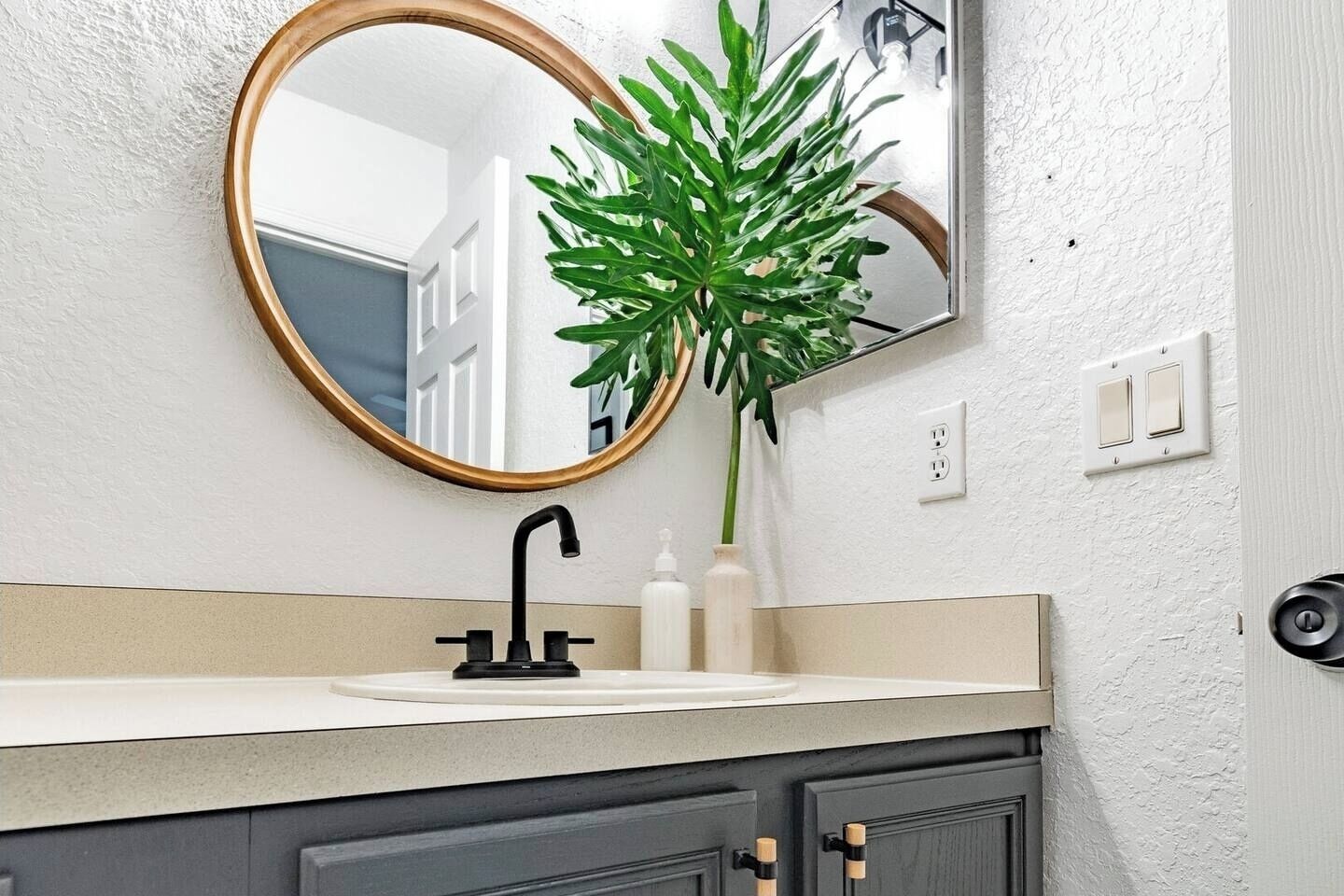 A bathroom with a round mirror, a black faucet, a white sink, and a potted plant.