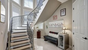 Eine Treppe mit geschwungener Geländer führt zu einer Zwischenebene. Dort befindet sich eine Couch mit Kissen und einer Lampe.