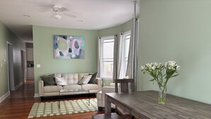 Ett vardagsrum med en beige soffa, ett matbord i trä och en vas med blommor.