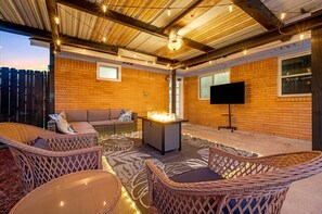 Een terras buiten met rieten meubels, een vuurkorf en een flatscreen televisie.