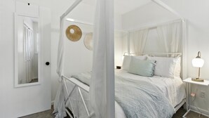 A bedroom with a canopy bed, a bedside table with a lamp, and a mirror on the wall. - Cozy Cottage Home in Mount Pleasant (Mount Pleasant)