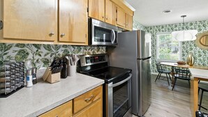 A kitchen with wooden cabinets, stainless steel appliances, a microwave, oven, and a refrigerator. There is a dining table with chairs and a window with blinds. - Cozy Cottage Home in Mount Pleasant (Mount Pleasant)