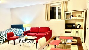 A compact room with a bed, red sofa, dining table, and kitchenette. - Entire basement with large windows, private full bathroom and office (Ottawa)
