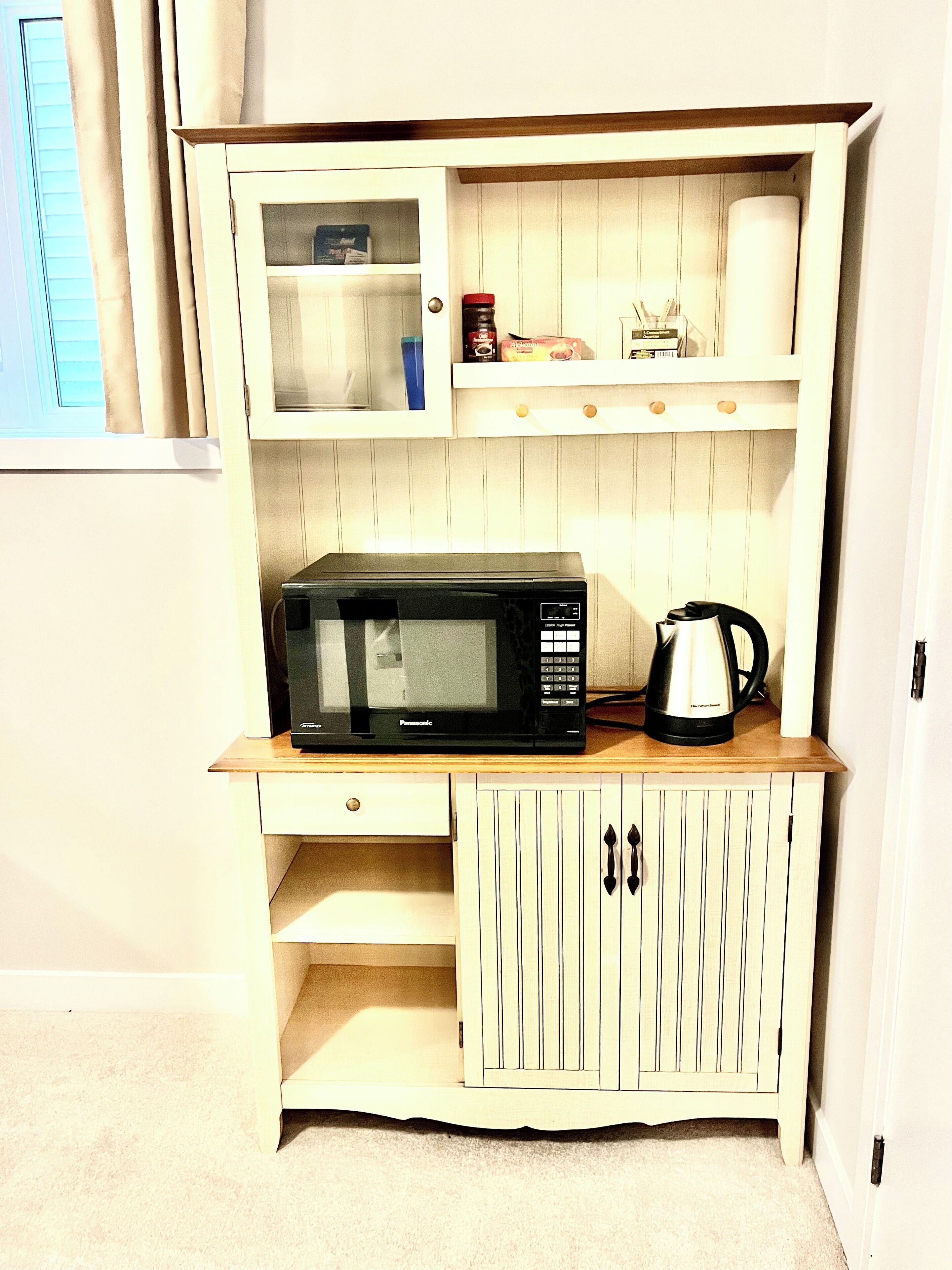 A kitchenette with a microwave, kettle, and storage cabinets.