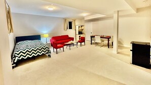 A hotel room with a bed, a red sofa, a dining table with chairs, a small table with a lamp, and a TV. - Entire basement with large windows, private full bathroom and office (Ottawa)