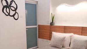 Un dormitorio con una cama, una mesita de noche, una lámpara de pared y un ventanal.