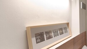 Una habitación moderna con cabecera de madera, una foto enmarcada con un cartel que dice 'Come in we're open', y una lámpara del techo.