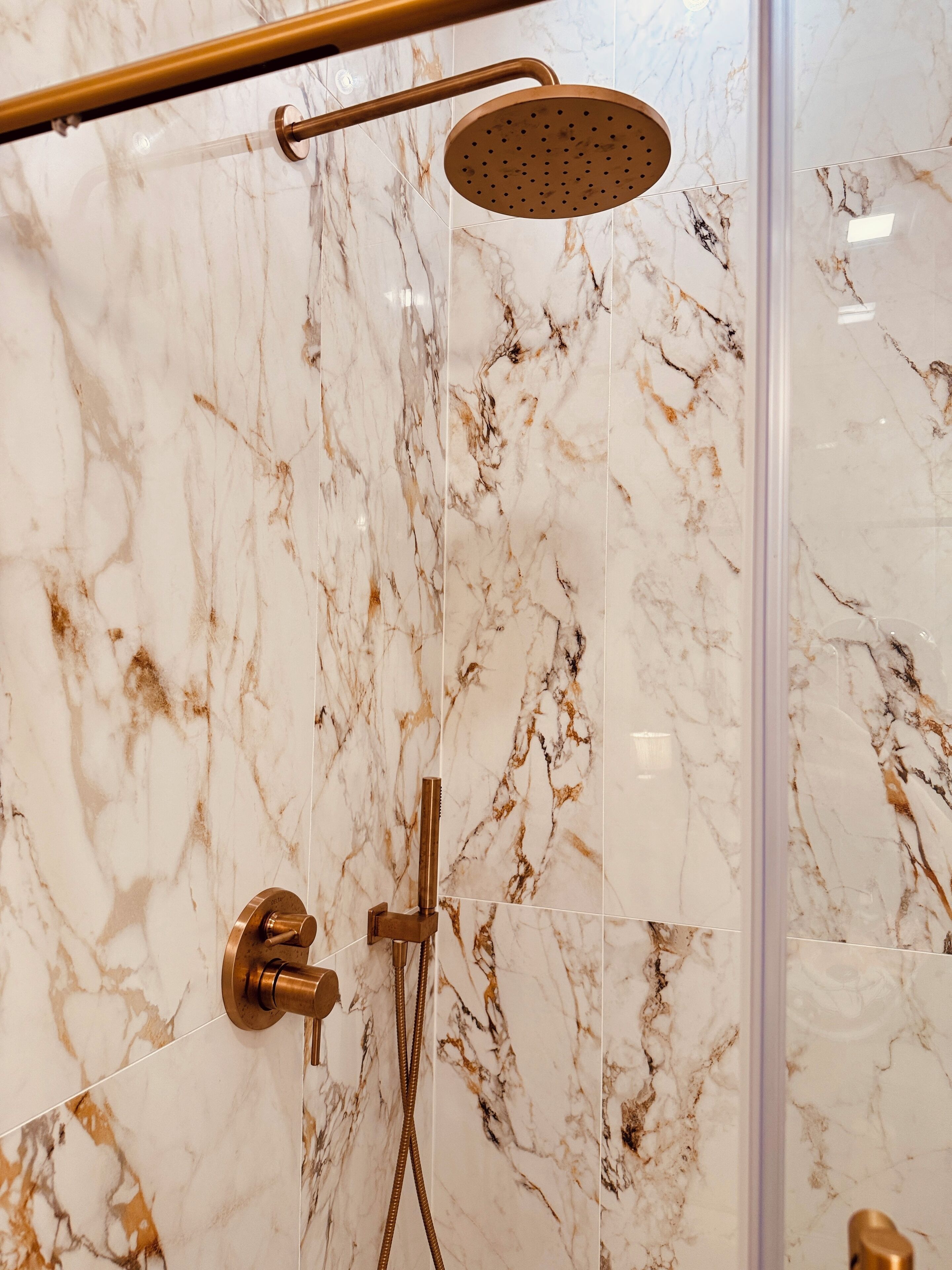 Une salle de bain moderne avec un mur en marbre, une pomme de douche dorée et un robinet doré.