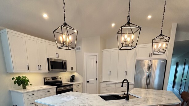 A modern kitchen with white cabinets, a central island with bar stools, stainless steel appliances, and pendant lighting. - Duplexes on Hawthorne (Dauphin)