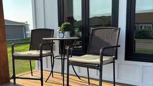 A wooden deck with two wicker chairs and a small table, featuring a white exterior wall and large windows. - Duplexes on Hawthorne (Dauphin)