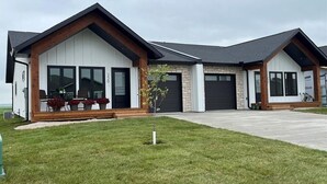 A modern two-story house with a garage, a covered patio, and a well-maintained lawn. - Duplexes on Hawthorne (Dauphin)