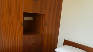 Ett sovrum med en garderob i trä, en säng med vita sängkläder och ett litet, inbyggt skrivbord med lådor.