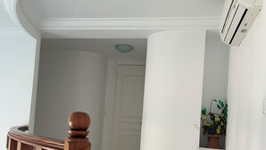 En hall med en trätrappa, en vit dörr och en väggmonterad luftkonditioneringsanläggning.