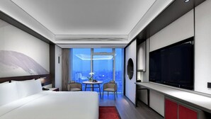 A modern hotel room with a large bed, a TV, a desk, and a city view.