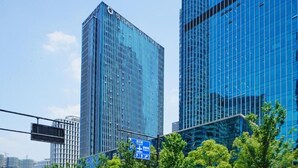 Two high-rise buildings with reflective glass facades, a clear blue sky, and a street sign in the foreground.