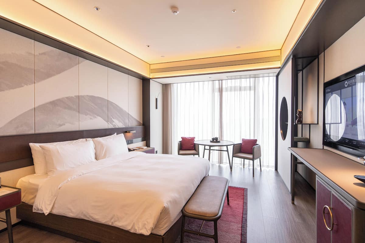 Une chambre d’hôtel moderne dotée d’un grand lit, d’un bureau, d’une chaise, d’une télévision et offrant une vue sur l’extérieur.