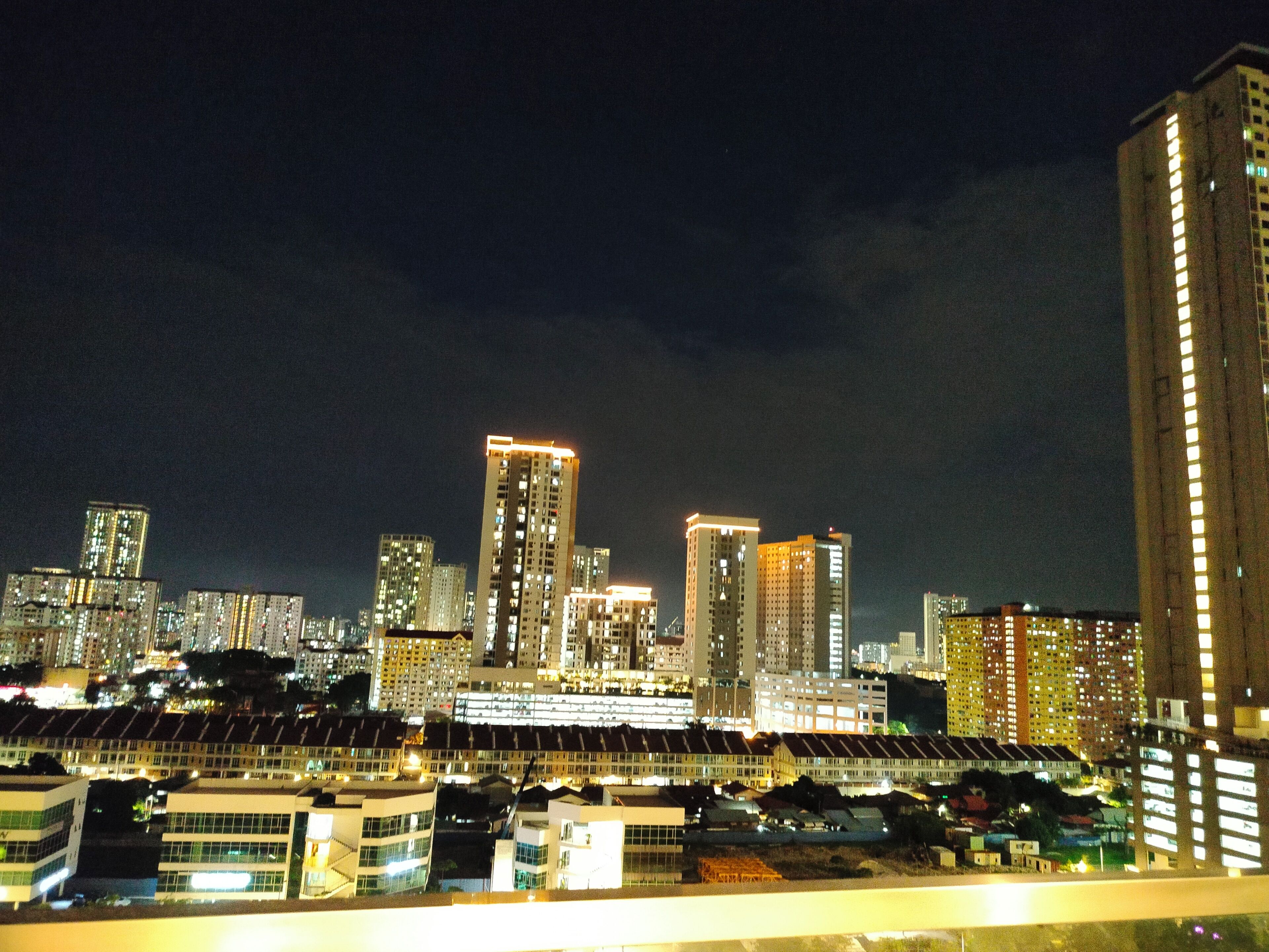 A nighttime cityscape with high-rise buildings and a row of modern, multi-story structures in the foreground.