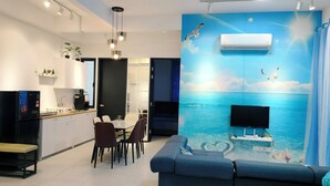 A modern living room with a large TV, a sofa, and a dining area with chairs and a table.