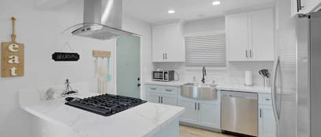 Una cocina moderna con gabinetes blancos, lavavajillas de acero inoxidable y microondas integrado.