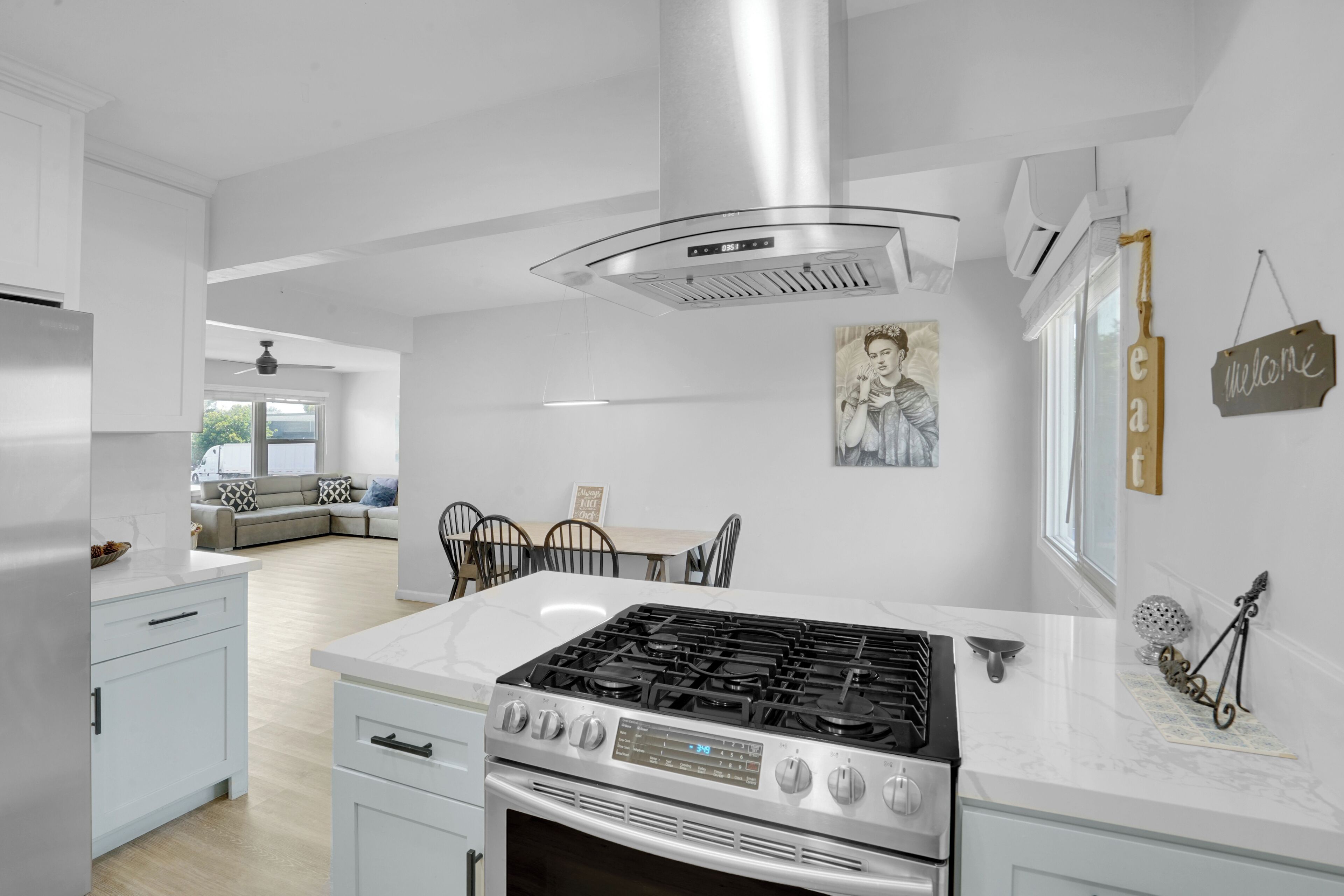 Una cocina moderna con estufa de acero inoxidable, armarios blancos y una zona de comedor con sofá y sillas.