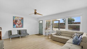 Ein geräumiges Wohnzimmer mit grauem Sofa, beigem Sofa und Deckenventilator.