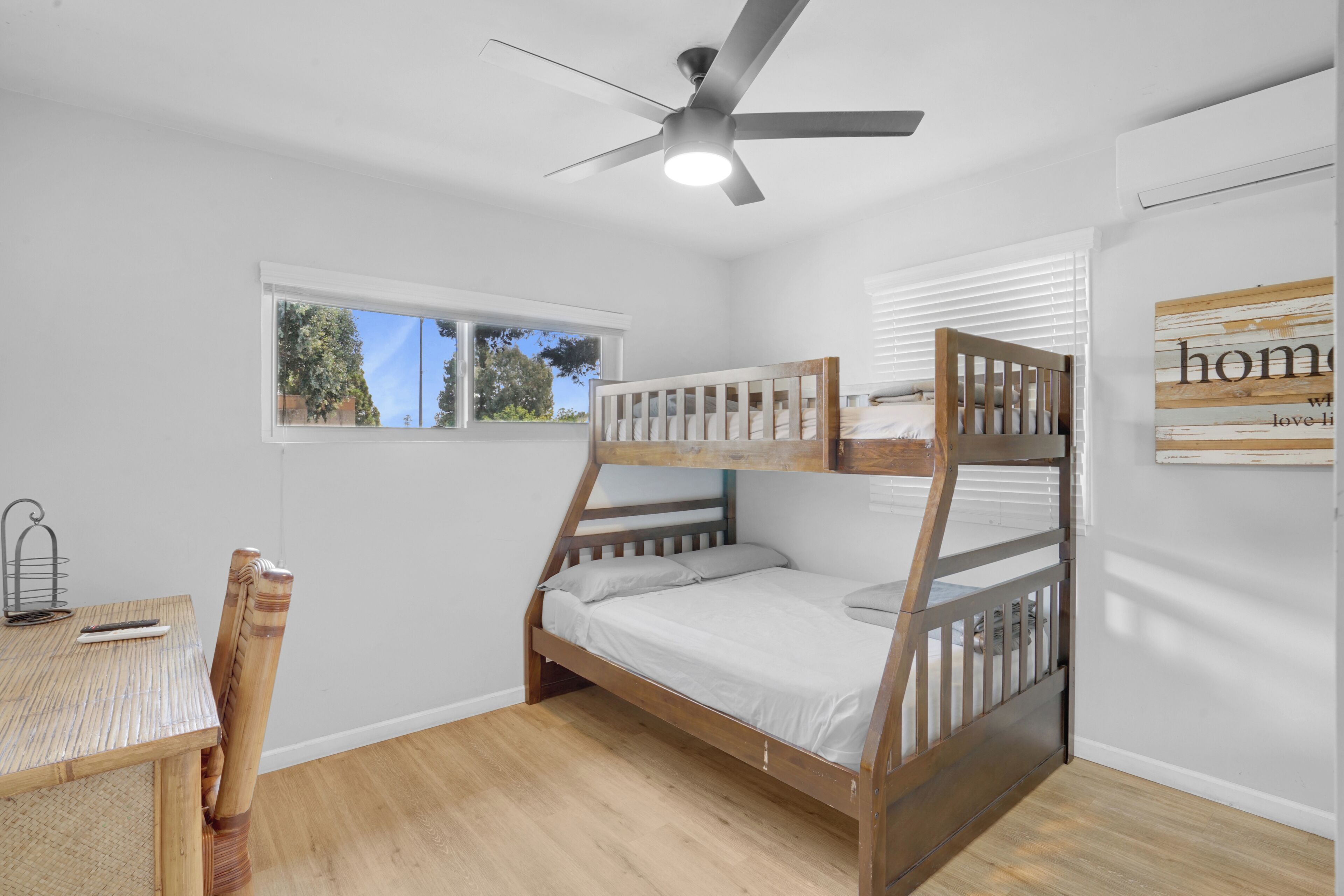 A bunk bed room with a ceiling fan, a window, a table with a chair, and a wall with a sign.