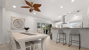 Cocina moderna con armarios blancos, una isla central y taburetes de bar.