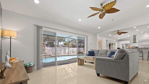 Una sala de estar moderna con un sofá gris, una mesa de centro de madera y un ventanal con acceso a una zona de piscina.