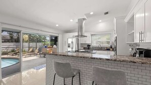 Una cocina moderna con una isla grande, taburetes de bar y vistas a una piscina y zona de estar exterior.