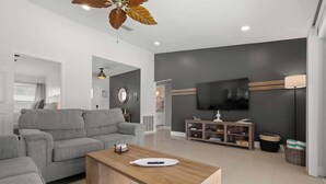 Una sala de estar moderna con un sofá gris, una mesa de centro de madera, un ventilador de techo, un televisor y una estantería.